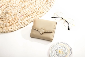 Close-up of small apricot leather wallet with clover metal clasp on woven placemat