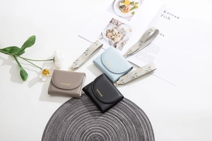Three minimalist tri-fold wallets in black, taupe, and blue with floral wrist straps