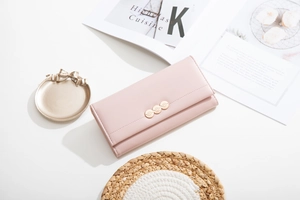 Detail view of light pink tri-fold long wallet with leaf-textured metal charms on leather