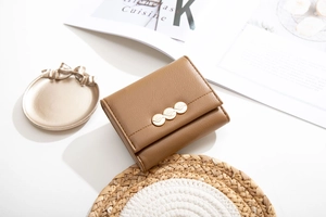 Detail of brown tri-fold wallet with golden leaf buckle and precise stitching on leather