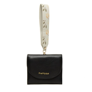 Detail of black faux leather wallet featuring a leaf-patterned wristlet strap and gold hardware