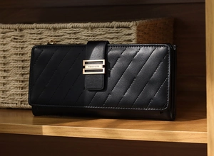 Detail of black quilted long wallet with golden buckle on a wooden shelf