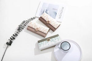 Three long PU leather wallets with leaf prints and round metal buckles on a white tabletop