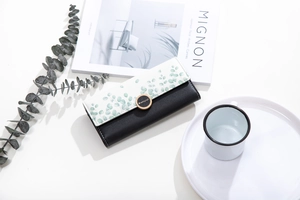 Detail of long tri-fold wallet with eucalyptus print, black leather and gold buckle