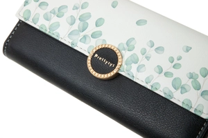 Close-up of trifold long wallet featuring leaf print pattern and gold logo buckle