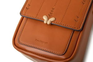 Détail de broderie de feuilles et fermoir papillon doré sur sac en cuir PU marron