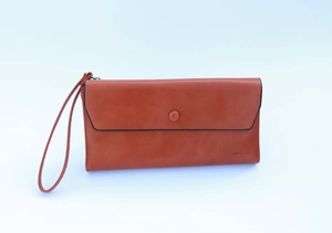 Detail of tan leather wristlet clutch with envelope flap and logo engraving