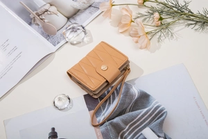 Detail of light brown quilted leather wallet with gold leaf buckle and wrist strap