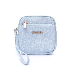Close-up of light blue textured fabric wallet featuring metal brand plaque and wristlet