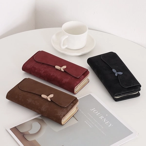 Three elegant long leaf-clasp wallets in burgundy, brown and black on a white table
