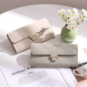 Detail of elegant wallets in beige and grey with a golden leaf buckle on a bright table
