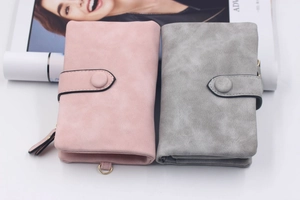 Detail view of pink and grey matte tri-fold wallets with metal buckle and side zipper