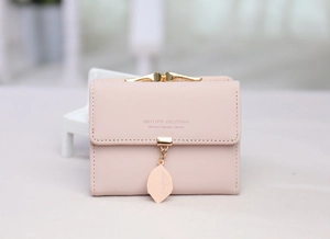 Close-up of pink tri-fold wallet featuring leaf pendant and golden metal clasp detail