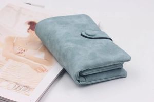 Detail of matte faux suede women's trifold wallet with button closure in dusty blue color