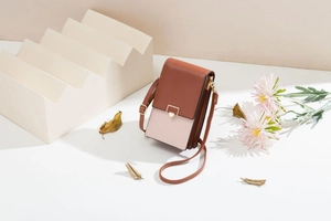 Detail of dual-tone leather phone bag with gold metal buckle on a white pedestal