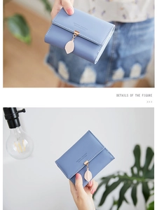 Close-up of a light blue tri-fold wallet featuring a delicate leaf pendant and snap closure