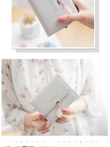 Macro detail of a light grey tri-fold wallet featuring a delicate pink leaf metal pendant