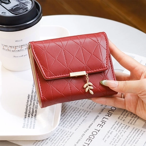 Détail du pendentif feuille bordeaux et texture matelassée sur un portefeuille compact