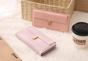 Top view of two long flap wallets with heart-shaped metal buckles on a soft white rug