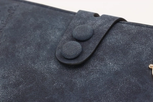 Macro shot of dark blue suede wallet flap with snap buttons and gold metal hardware
