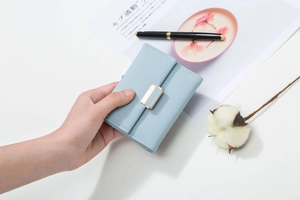 Detail of light blue tri-fold wallet with quilted pattern and gold metal buckle