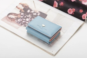 Close-up of light blue trifold wallet with gold heart buckle on a fashion magazine