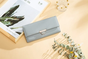 Detail of light blue leather wallet with heart-shaped gold clasp on a beige tabletop
