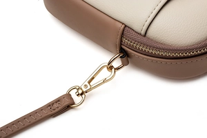 Detail of light gold hardware clasp and stitching on a two-tone leather mini crossbody bag