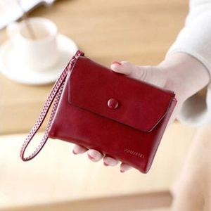 Red small leather wallet with snap closure and wrist strap held over a wooden table