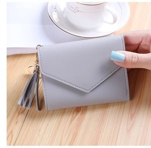 Close-up of grey leather envelope wallet with tassel and heart charm held by hand