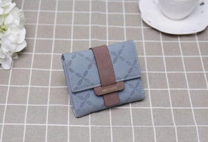 Gros plan d'un portefeuille bleu avec relief floral et fermoir marron sur gris