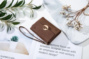 Brown leather wallet with floral embossing and gold C-shaped metal buckle on marble tray