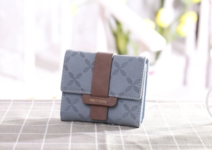 Vue détaillée du portefeuille matelassé bleu-gris avec lanière en cuir brun et trèfles gaufrés