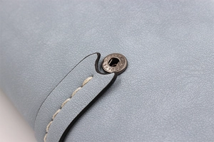 Detail of light blue textured leather wallet with white stitching and bronze snap button