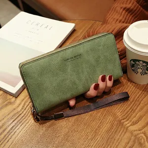 Détail d'un portefeuille long en cuir vert avec fermeture éclair et dragonne sur bois
