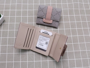 Détail d'un portefeuille compact à trois volets montrant l'extérieur gris et le fermoir rose