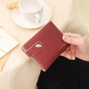 Detail of burgundy leather wallet showing precise white stitching and gold leaf accent