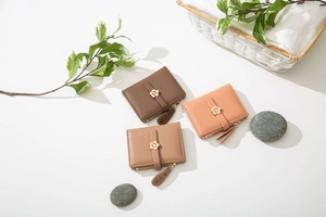 Drei minimalistische Kurzgeldbörsen in Braun, Hellbraun und Rosa mit goldener Blumenschließe