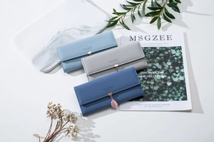 Three long PU leather wallets in blue and grey with leaf pendants on a marble surface