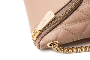 Détail d'un sac bandoulière beige matelassé avec fermeture éclair dorée et chaîne chic