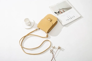 Detail der gelben gesteppten Handytasche mit goldenem Herzverschluss auf einem Tisch