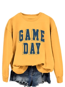 Close-up of GAME DAY embossed navy blue lettering on a mustard yellow crewneck sweatshirt