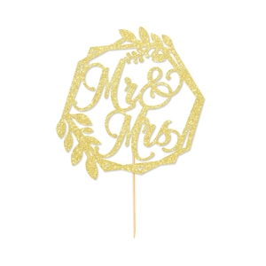 Close-up of golden glitter Mr & Mrs cake topper with hexagon frame and leaf accents