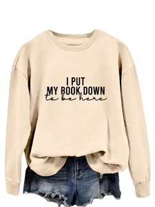 Close-up of beige crewneck sweatshirt with 'I PUT MY BOOK DOWN' print and ribbed cuffs