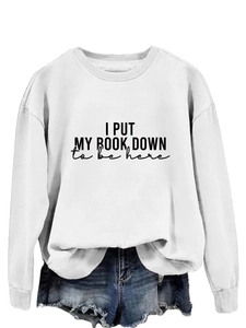 Detail of white crewneck sweatshirt featuring black I PUT MY BOOK DOWN artistic print