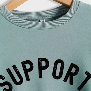 Close-up of grey-green crewneck sweatshirt with Support letter print on wood hanger
