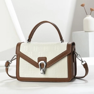 Détail d'un sac bandoulière minimaliste en cuir crème et marron avec une boucle argentée