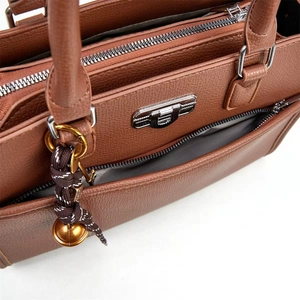 Detailed shot of brown pebble leather handbag with silver zipper and decorative charm