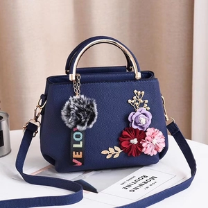 Sac bandoulière bleu marine avec fleurs et poignée dorée sur table blanche