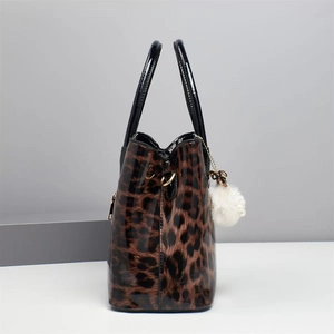 Detail of leopard print tote bag with black handles and white fuzzy pom pom keychain charm